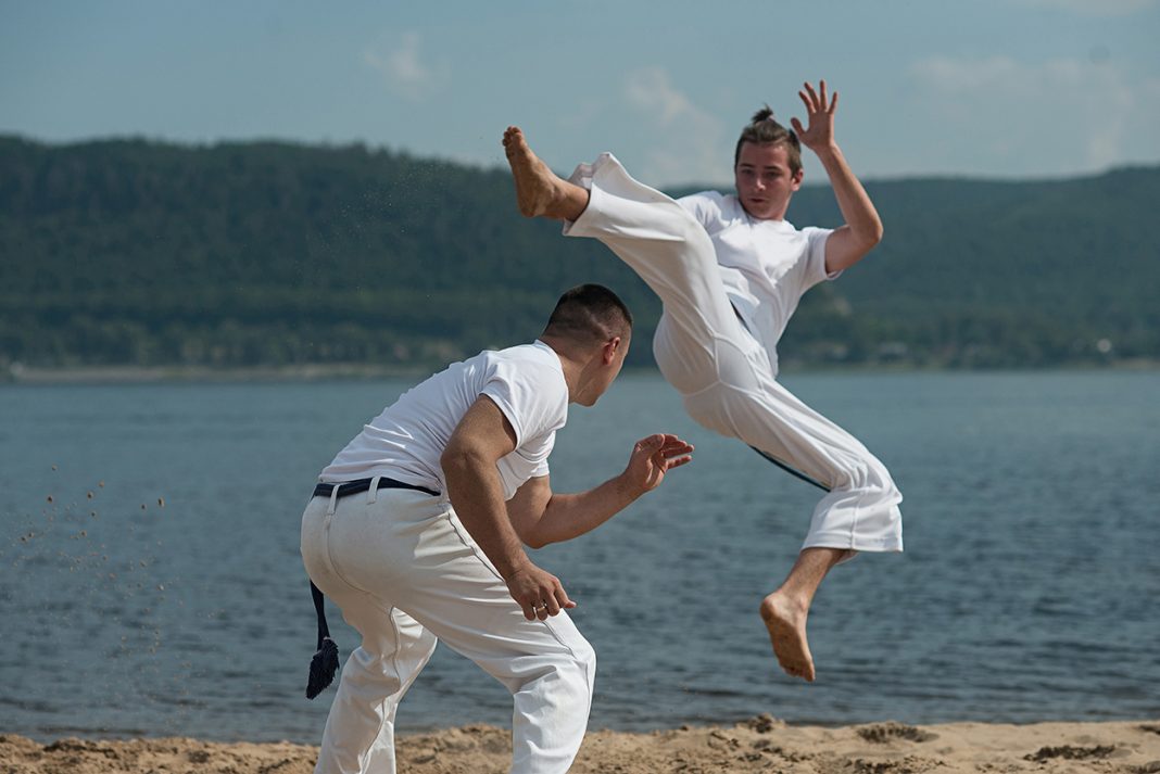 Men train capoeira on the beach - concept about people, lifestyle and sport.